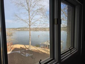 A view through a window of a lake with a tree and a small structure on the shore. - Peaceful Lakefront Retreat | 5* View, Dock, Games (Eatonton)