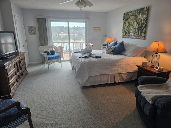 Ein Schlafzimmer mit Bett, Fernseher, Sessel, Lampe und Seeblick.