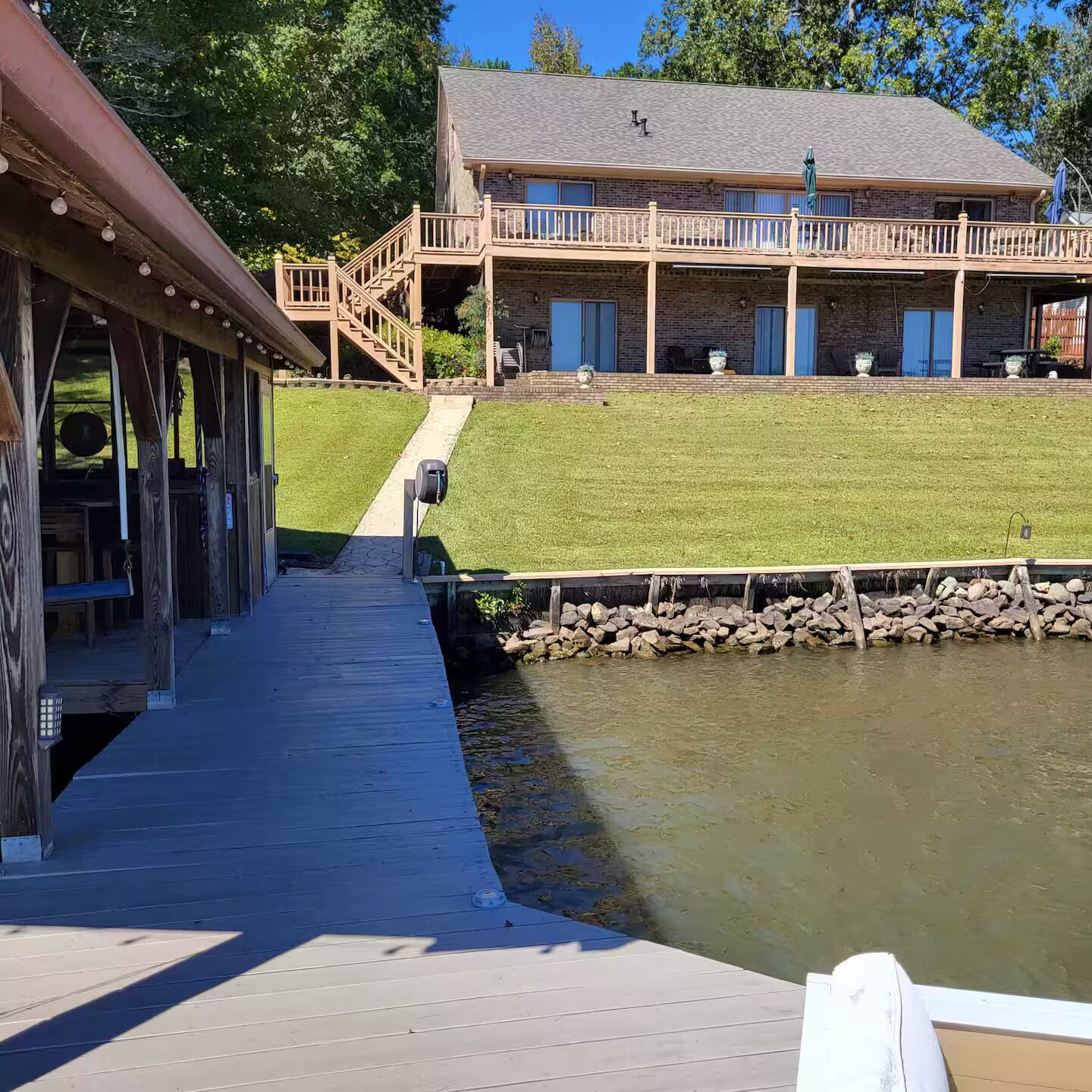 A wooden deck leading to a building with a stone foundation, a grassy area, and a body of water.