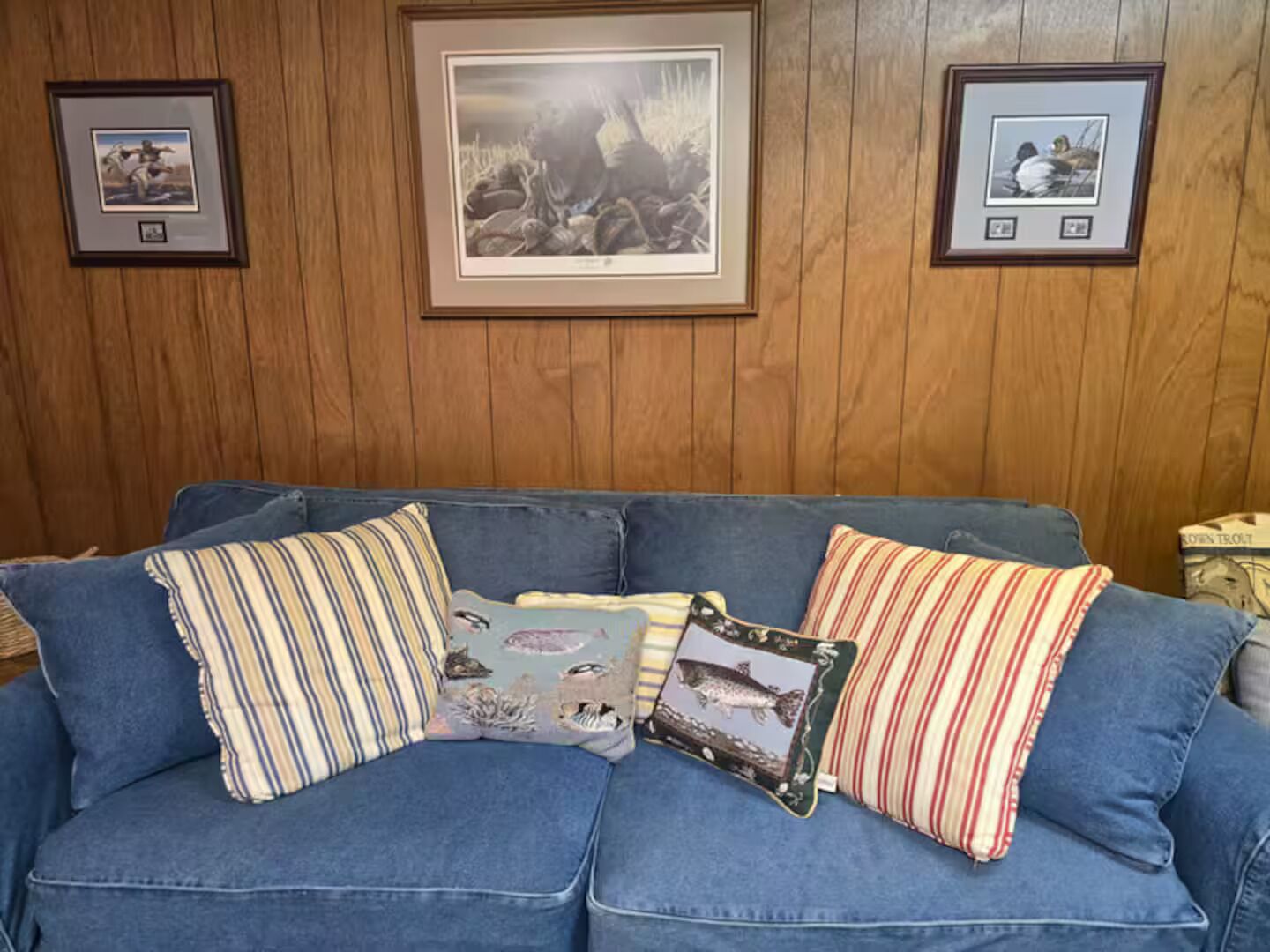 A blue sofa with striped and patterned cushions, framed pictures on the wall, and a wooden panel background.