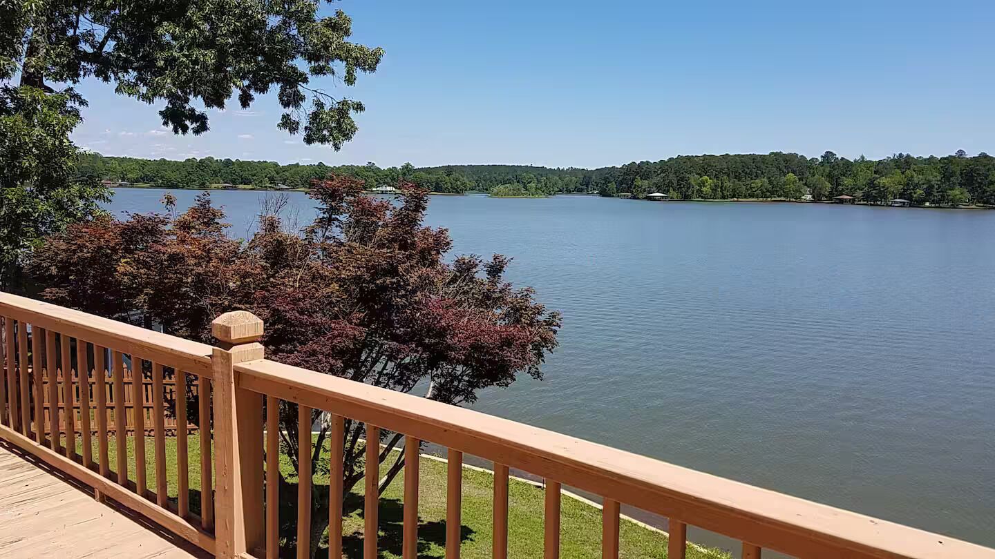 A wooden deck overlooking a calm lake with a distant forested hill.