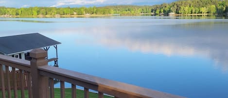 A deck with a view of a calm lake, surrounded by trees and a clear sky.