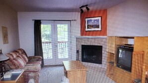 Ein Wohnzimmer mit einer Couch, einem kleinen Tisch, einem Kamin und einem Fernseher.