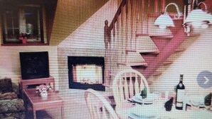 Ein Wohnzimmer mit Kamin, einem Esstisch mit Stühlen und einer Treppe, die zu einer oberen Etage führt.