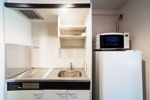 Una kitchenette compacta con un lavamanos de acero inoxidable, un microondas y un refrigerador.