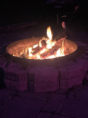 A circular fire pit with burning logs, surrounded by a brick border.