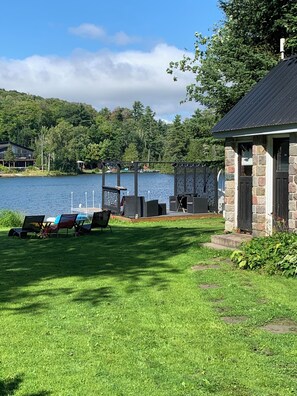 A lakeside property with a grassy lawn, outdoor seating, and a stone building.