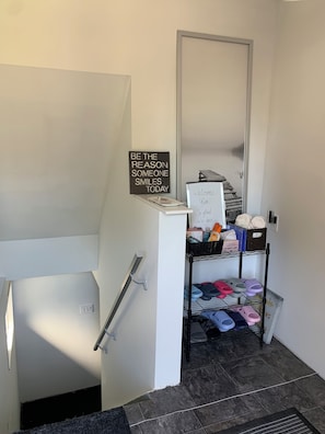 A hallway with a handrail, a sign with a motivational quote, a welcome sign, and a shoe rack with various slippers.