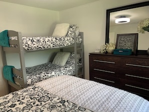A bunk bed with floral bedding, a dresser with drawers, and a mirror with a floral arrangement.