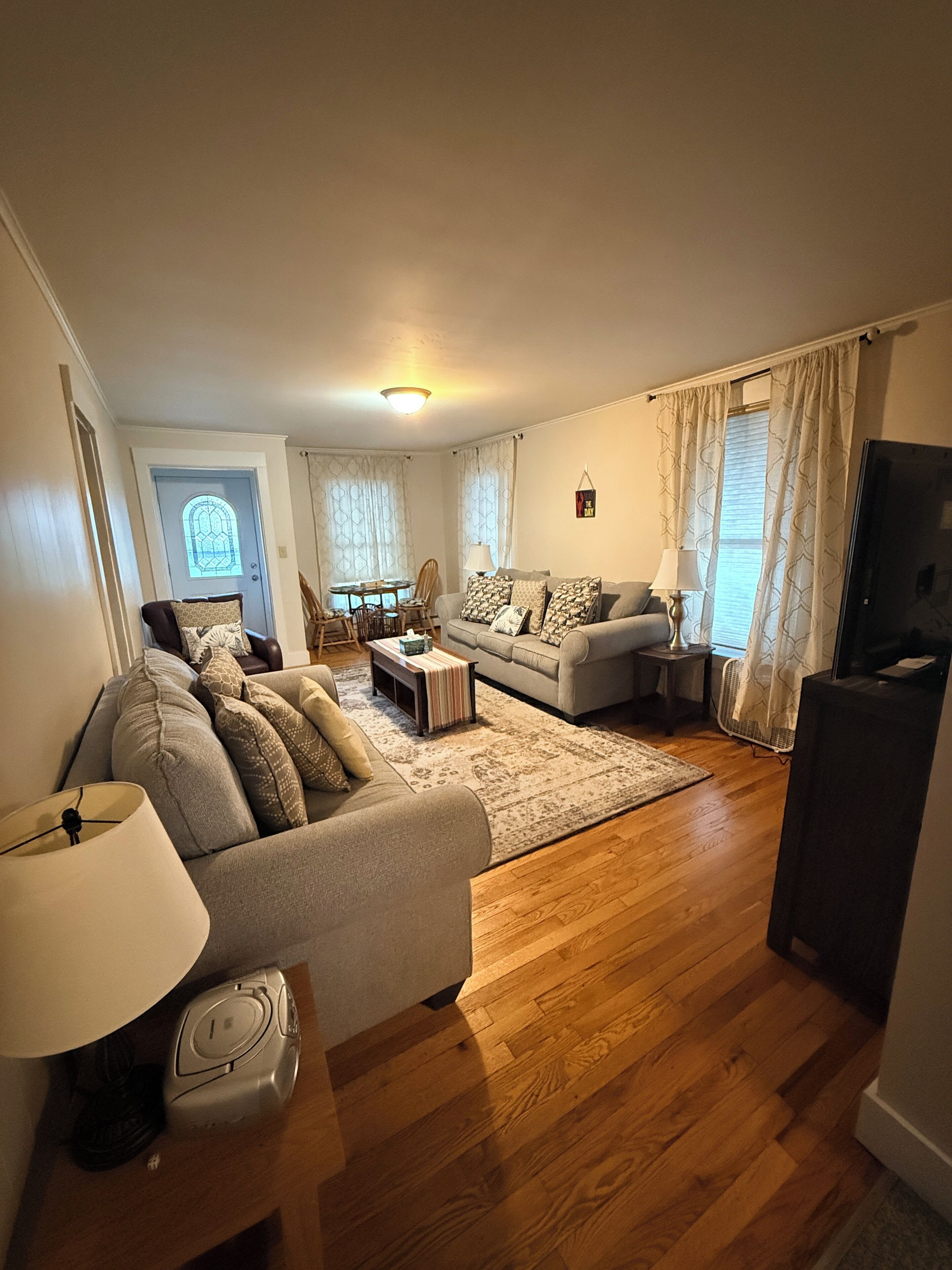A living room with a sofa, a coffee table, a TV stand, and a dining area with chairs and a table.