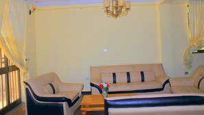 A hotel room with a sofa, a chair, a small table, and a chandelier. - Abusera Bishoftu Guest House (Dukem)