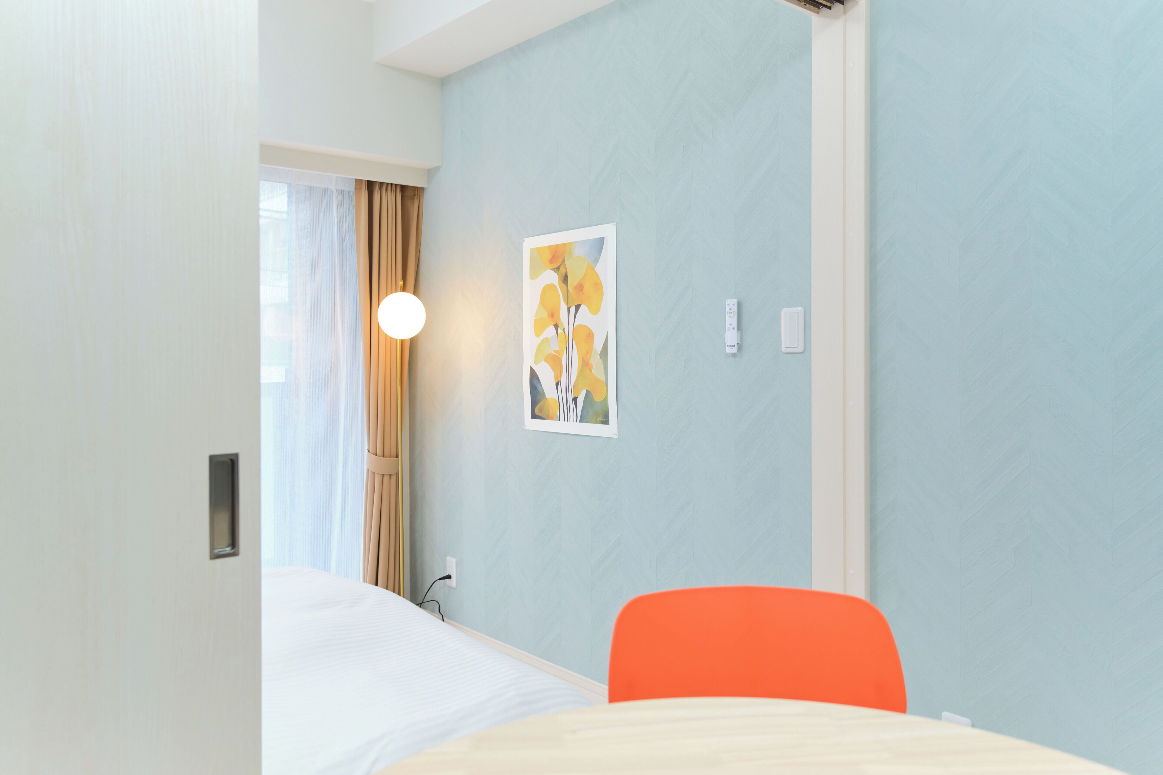 Une chambre d’hôtel avec un lit, une chaise, une lampe fixée au mur et un tableau.