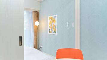 Une chambre d’hôtel avec un lit, une chaise, une lampe fixée au mur et un tableau.