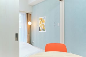 Une chambre d’hôtel avec un lit, une chaise, une lampe fixée au mur et un tableau.