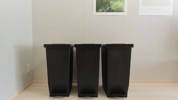 Trois poubelles noires sont alignées contre un mur, et deux œuvres d’art encadrées sont accrochées au-dessus.