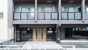 Un immeuble à plusieurs étages au design moderne, doté d’une entrée centrale avec une porte en bois, d’un espace extérieur aménagé et couvert, et d’un balcon situé aux étages supérieurs.