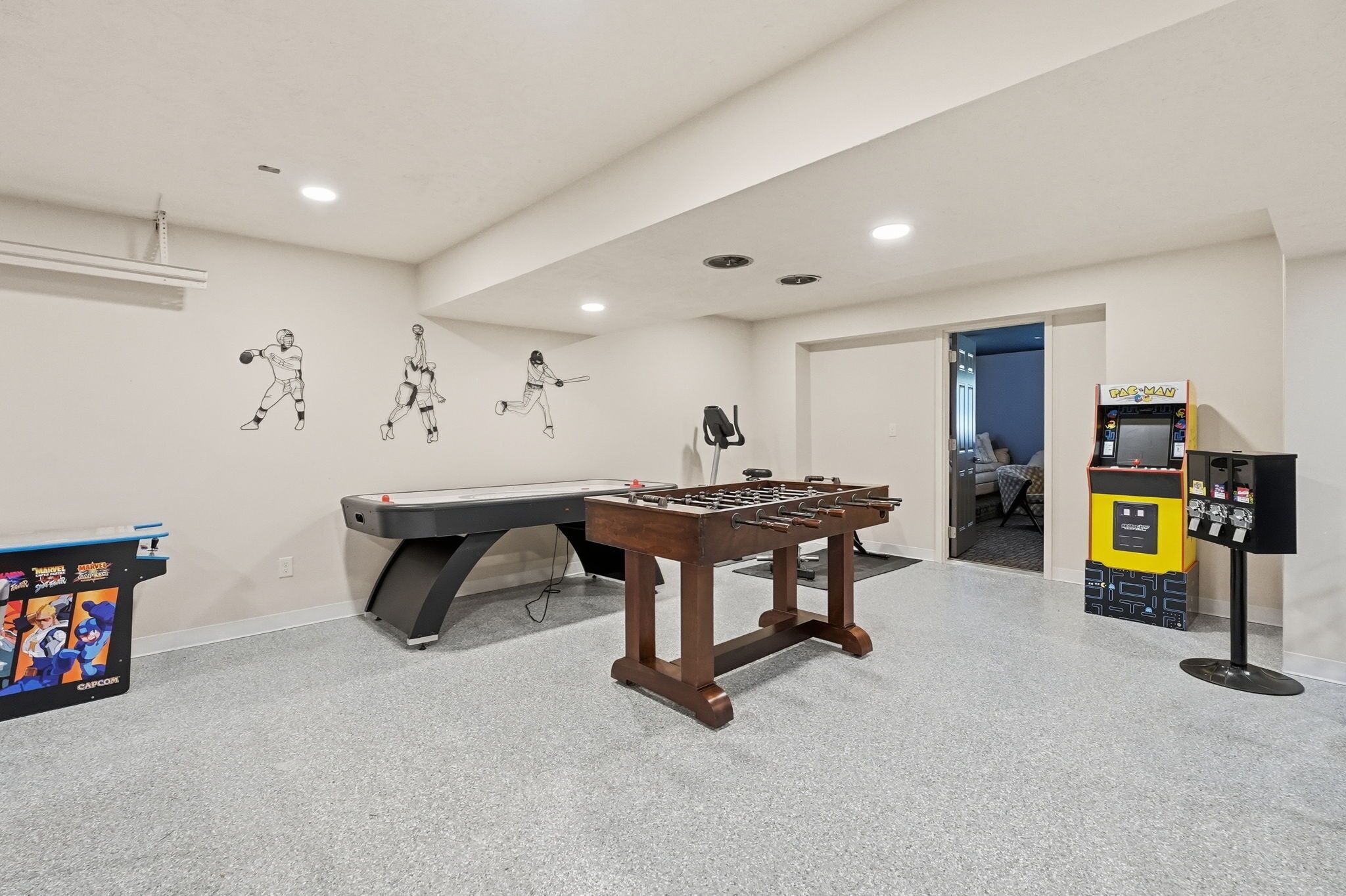 A room with a foosball table, a pool table, and a Capcom arcade machine.