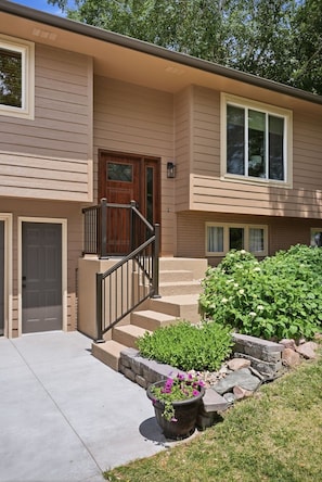 A two-story house with a front door, a small porch, a staircase, and a flower planter. - The Fellowship House: Large Groups - Hot Tub - Theater - Game Room - Fire Pit (Sioux Falls)