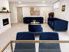 Una sala de estar con chimenea, un sofá azul, una mesa de centro redonda y una lámpara de pie.