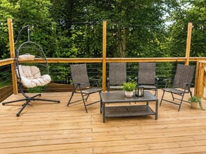 Una terraza de madera con una hamaca colgante, cuatro sillas, una mesa y una planta en maceta.