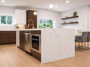 Una cocina moderna con una isla de mármol, electrodomésticos de acero inoxidable, armarios de madera y una lámpara colgante.