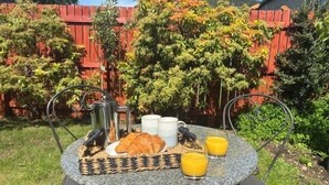 Ett runt bord med frukostmat, en metallstol och ett rött staket i bakgrunden.