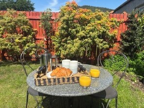 Ein runder Tisch mit Frühstücksangeboten, ein Metallstuhl und ein roter Zaun im Hintergrund.