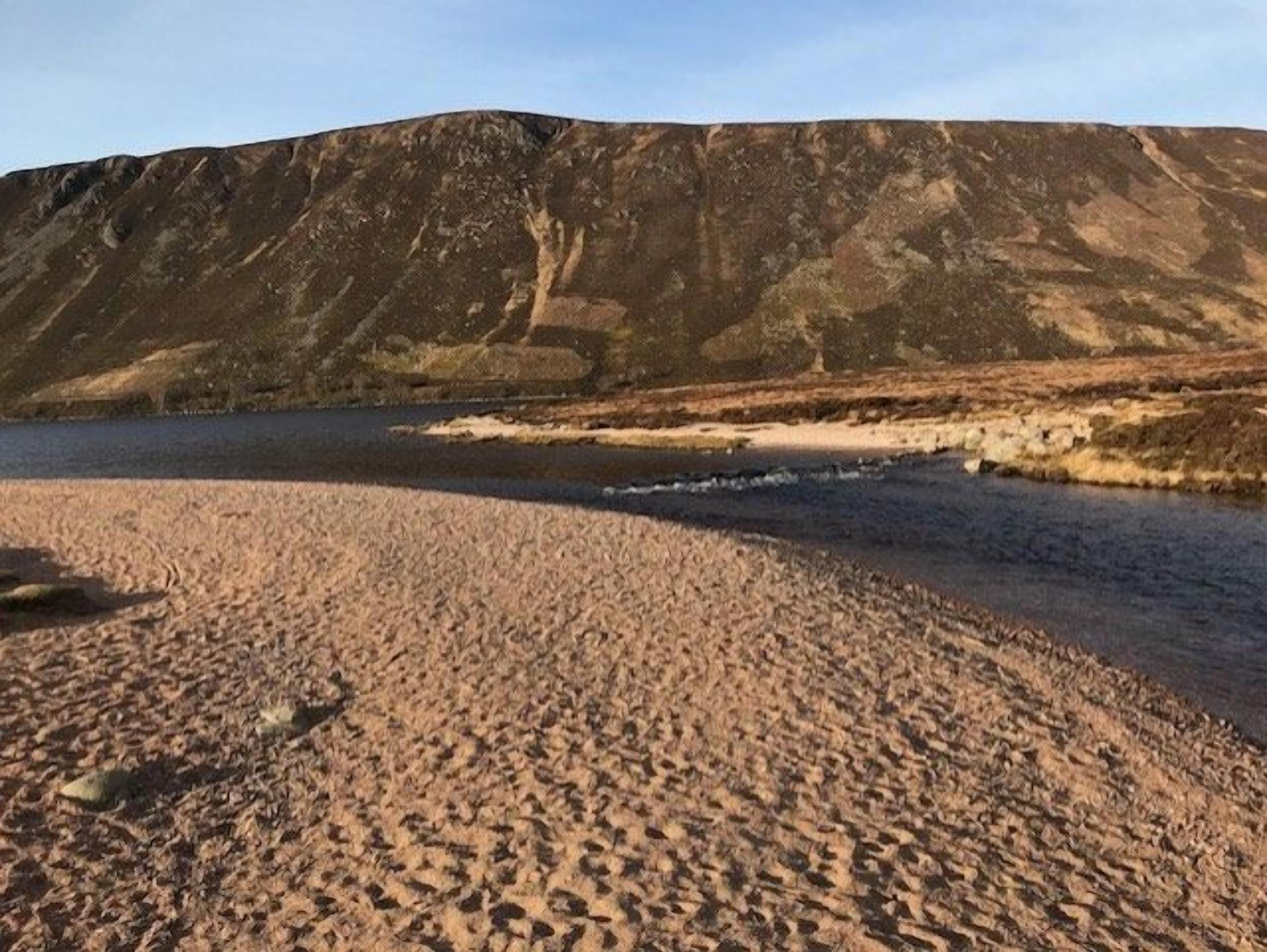 A beach with a river and a hill in the background.