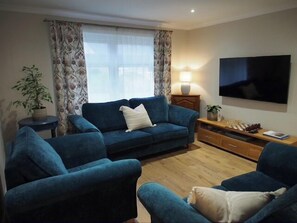 Ein Wohnzimmer mit einer Couch, zwei Sesseln, einem Fernseher, einer Lampe und einem Schachbrett.
