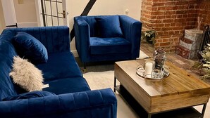 Una sala de estar con un sofá azul, una mesa de centro de madera, un reloj y una chimenea de ladrillo.