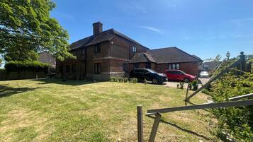 A brick house with a large yard, two cars parked in the driveway, and a wooden fence in the foreground.