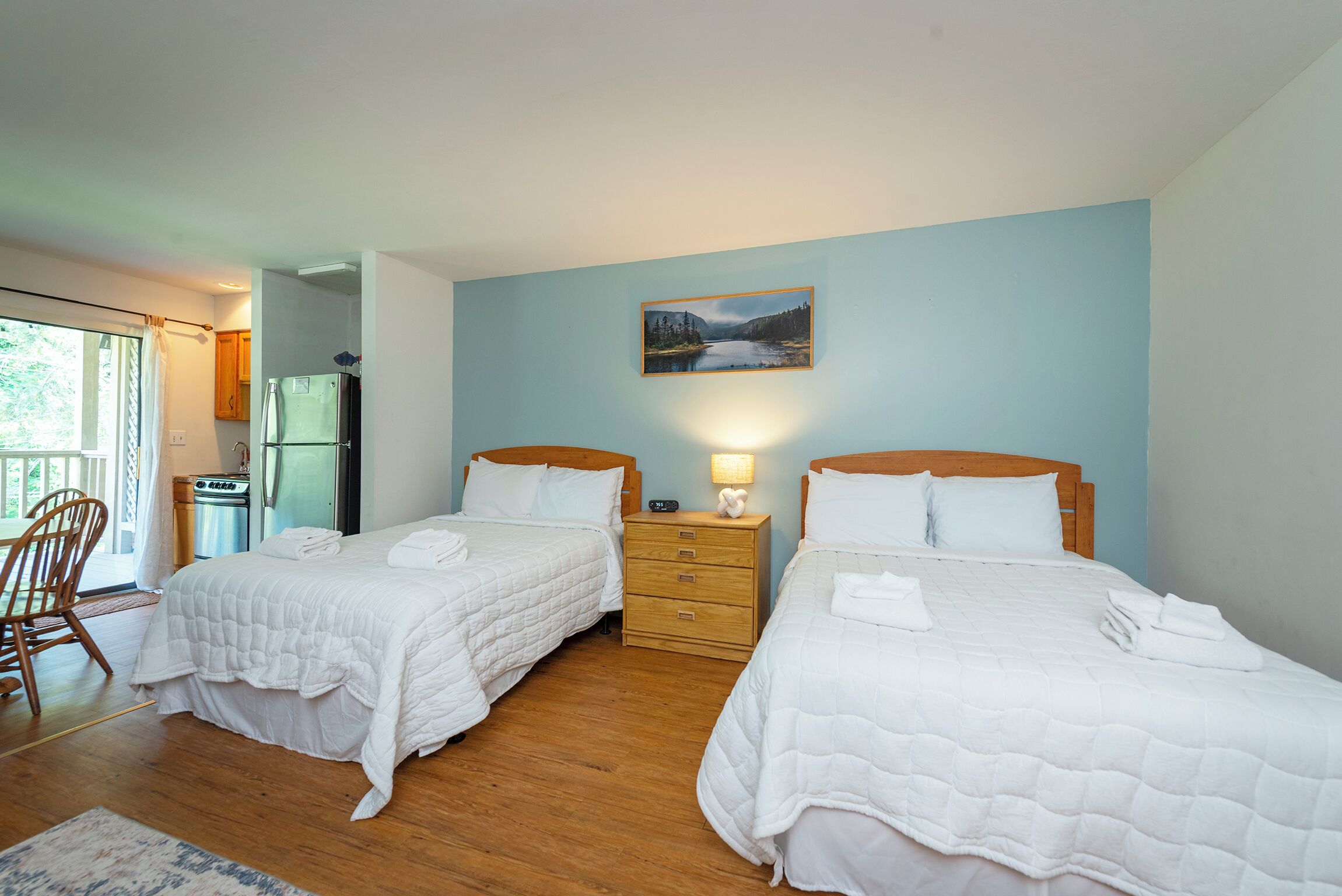 A room with two beds, a wooden dresser, a refrigerator, and a window with curtains.