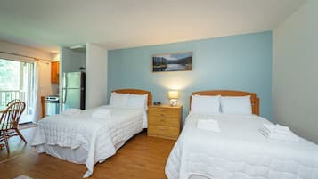 A room with two beds, a wooden dresser, a refrigerator, and a window with curtains.