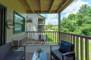 A covered porch with two wicker chairs, a small table with a vase of flowers, and a view of a green lawn and trees. - Apple Valley 7 at Rumbling Bald (Lake Lure)