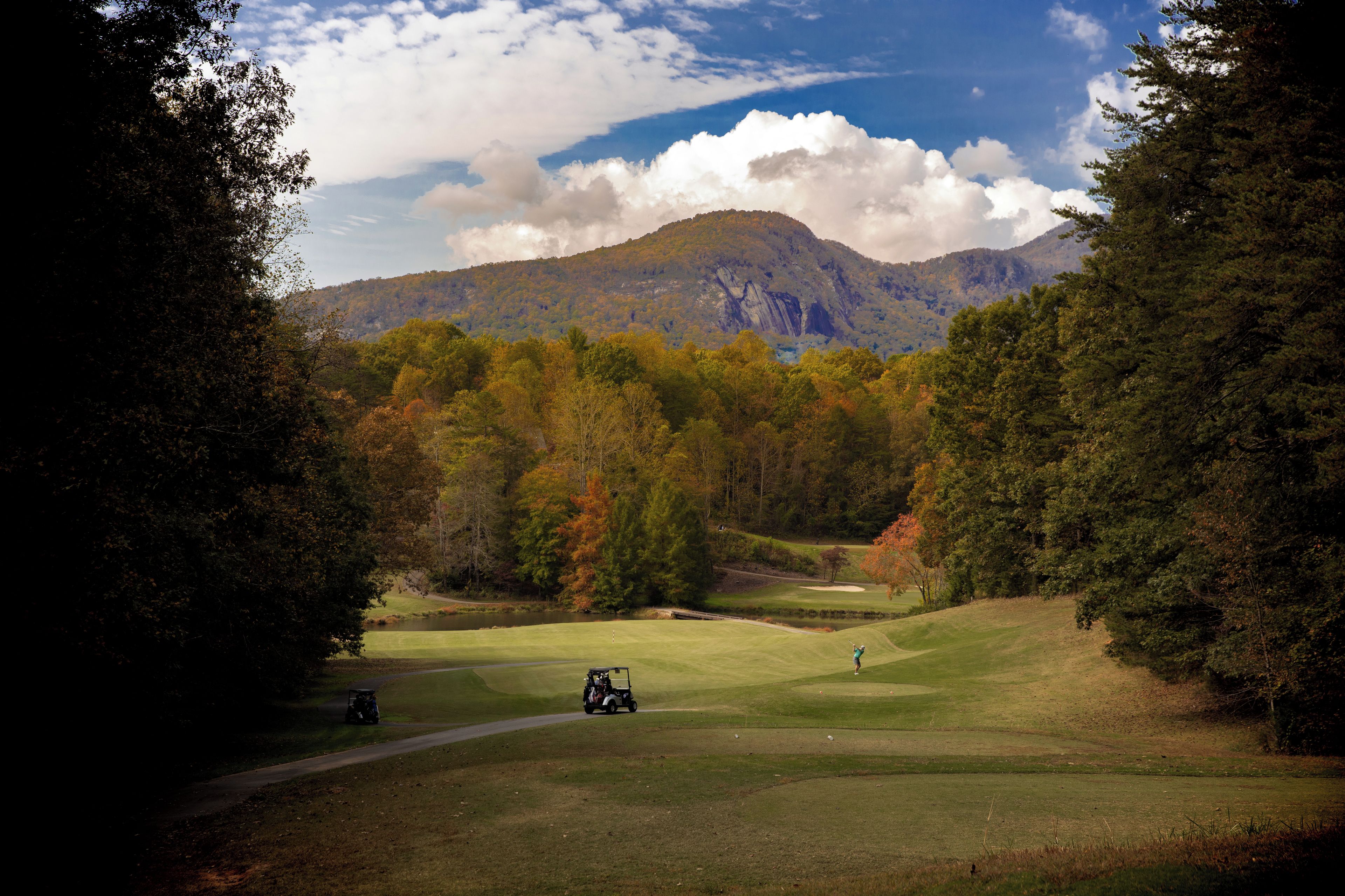 Ein Golfplatz mit Bergblick, einem Teich und blauem Himmel.