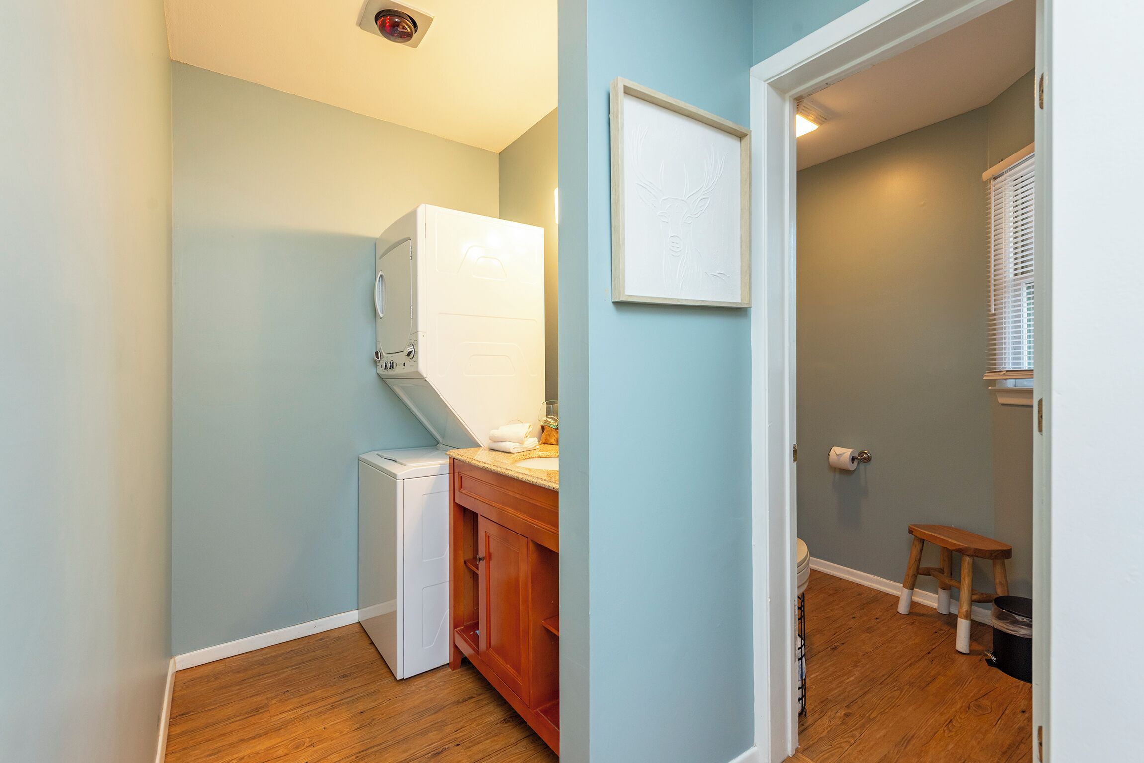 A compact kitchen with a built-in washer, wooden cabinets, and a small stool.