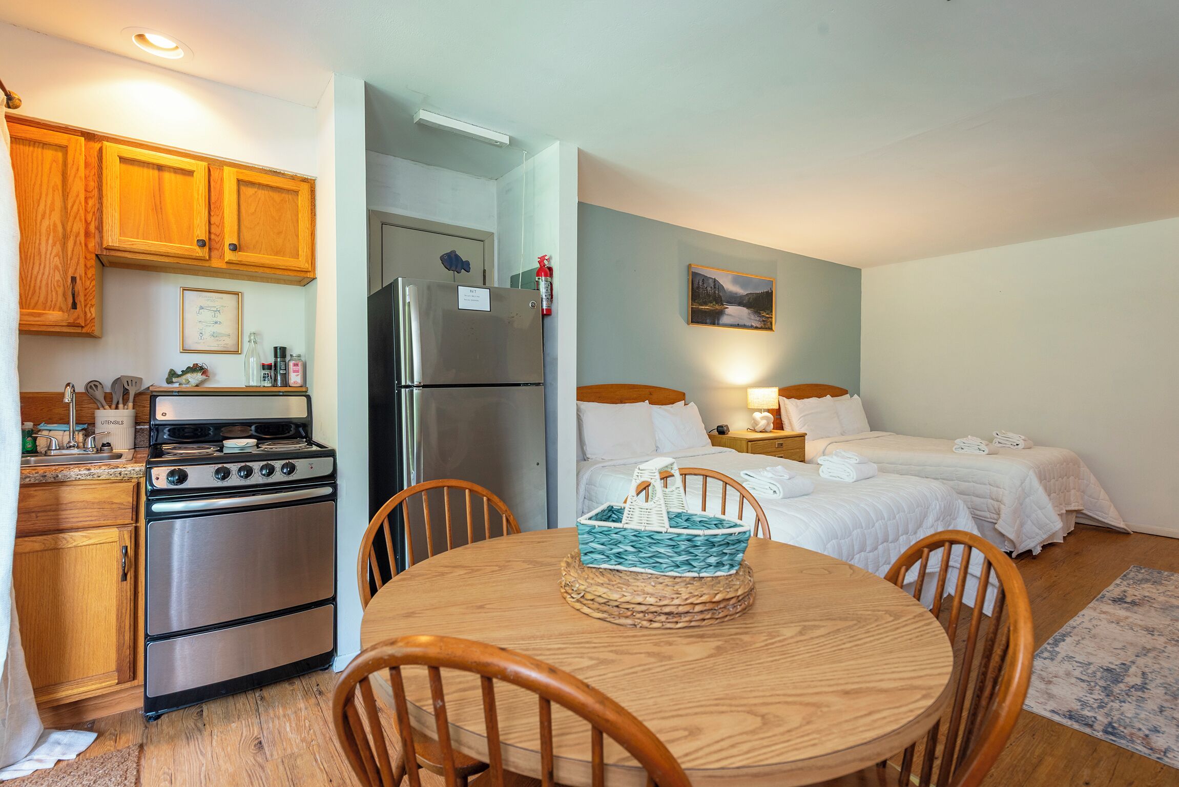 A compact hotel room with a kitchenette, a dining area, and a bed with two pillows.