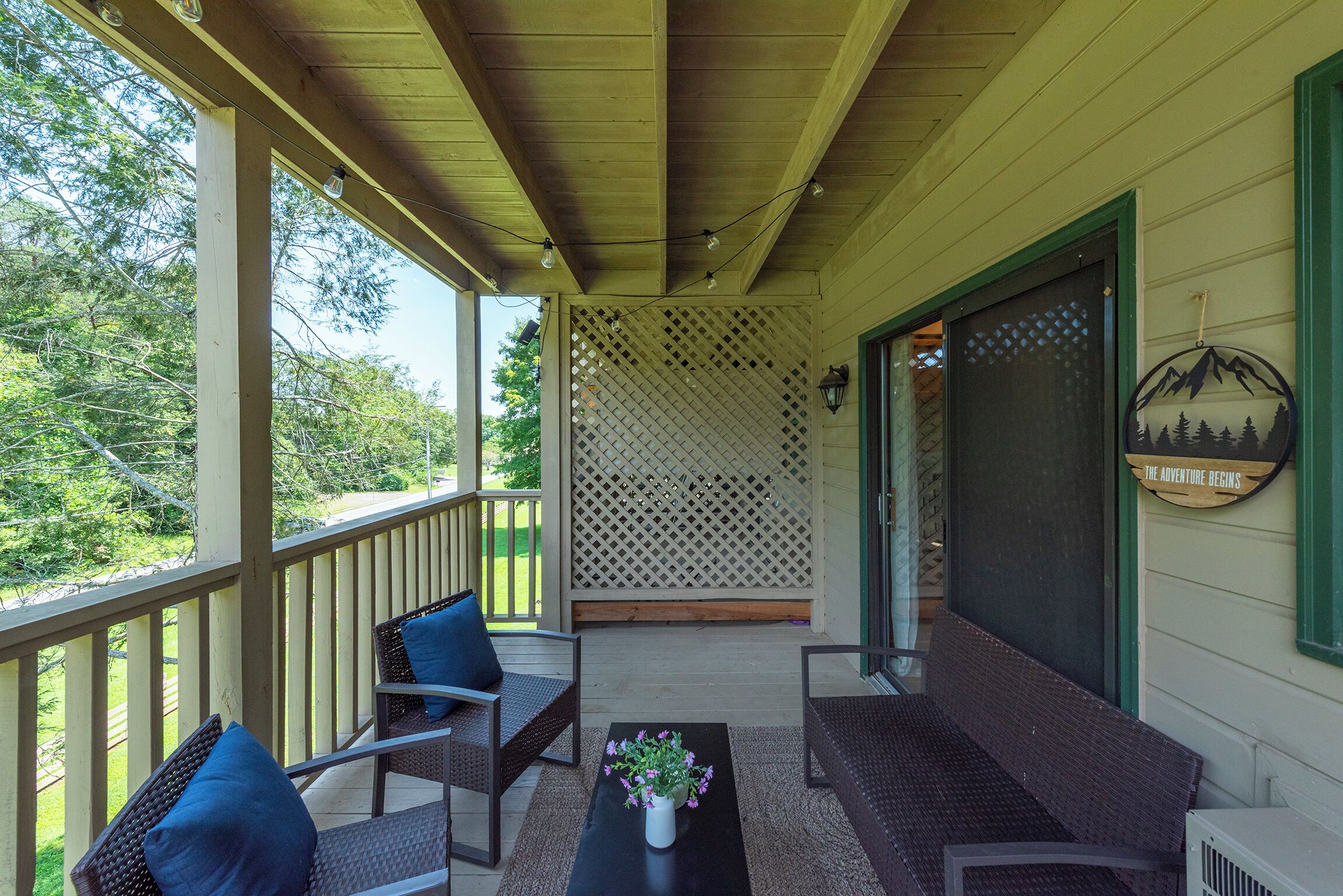 A covered porch with wicker furniture, a potted plant, and a decorative wall.