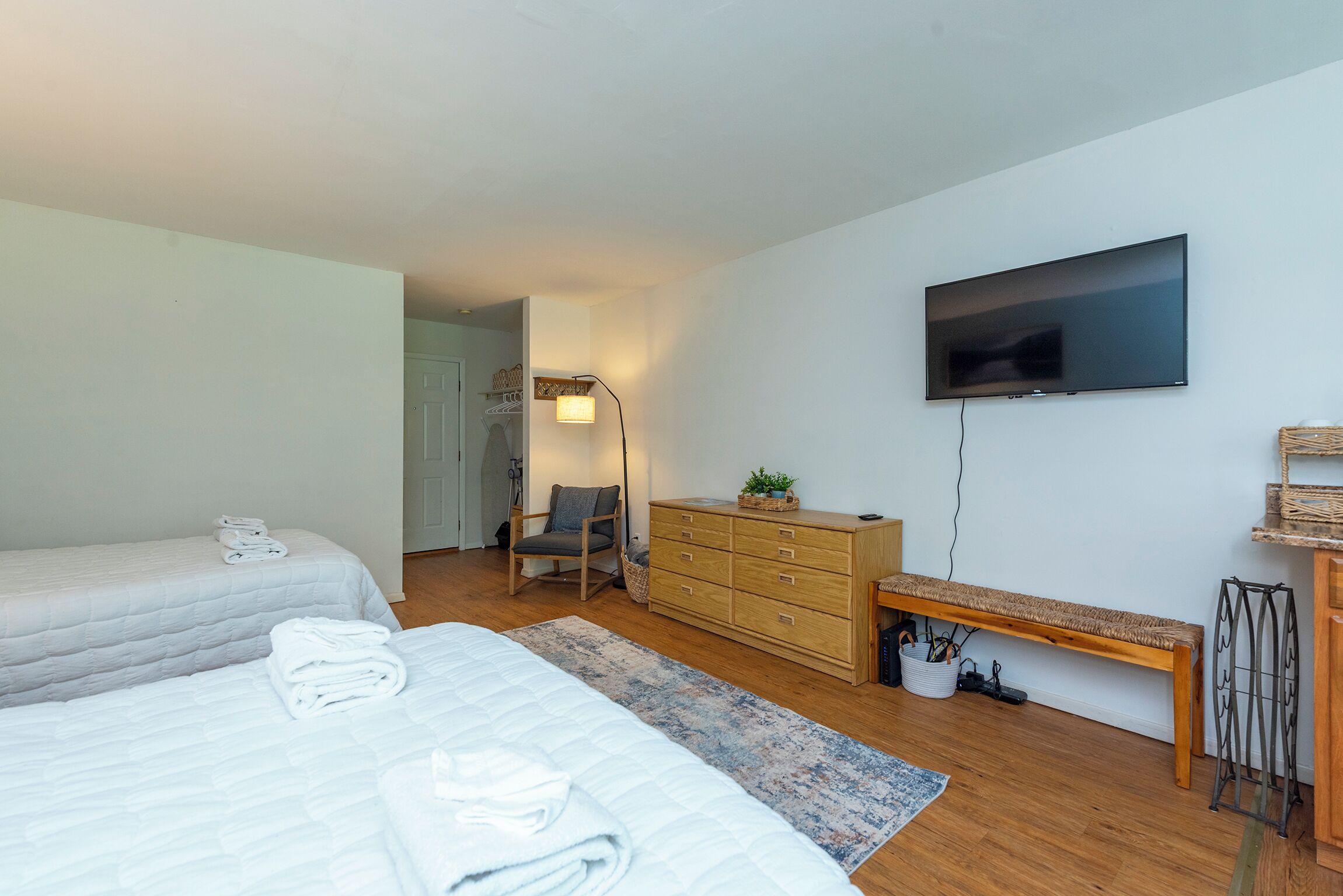 A bedroom with two beds, a dresser, a bench, a TV, and a lamp.