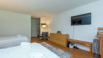 A bedroom with two beds, a dresser, a bench, a TV, and a lamp.