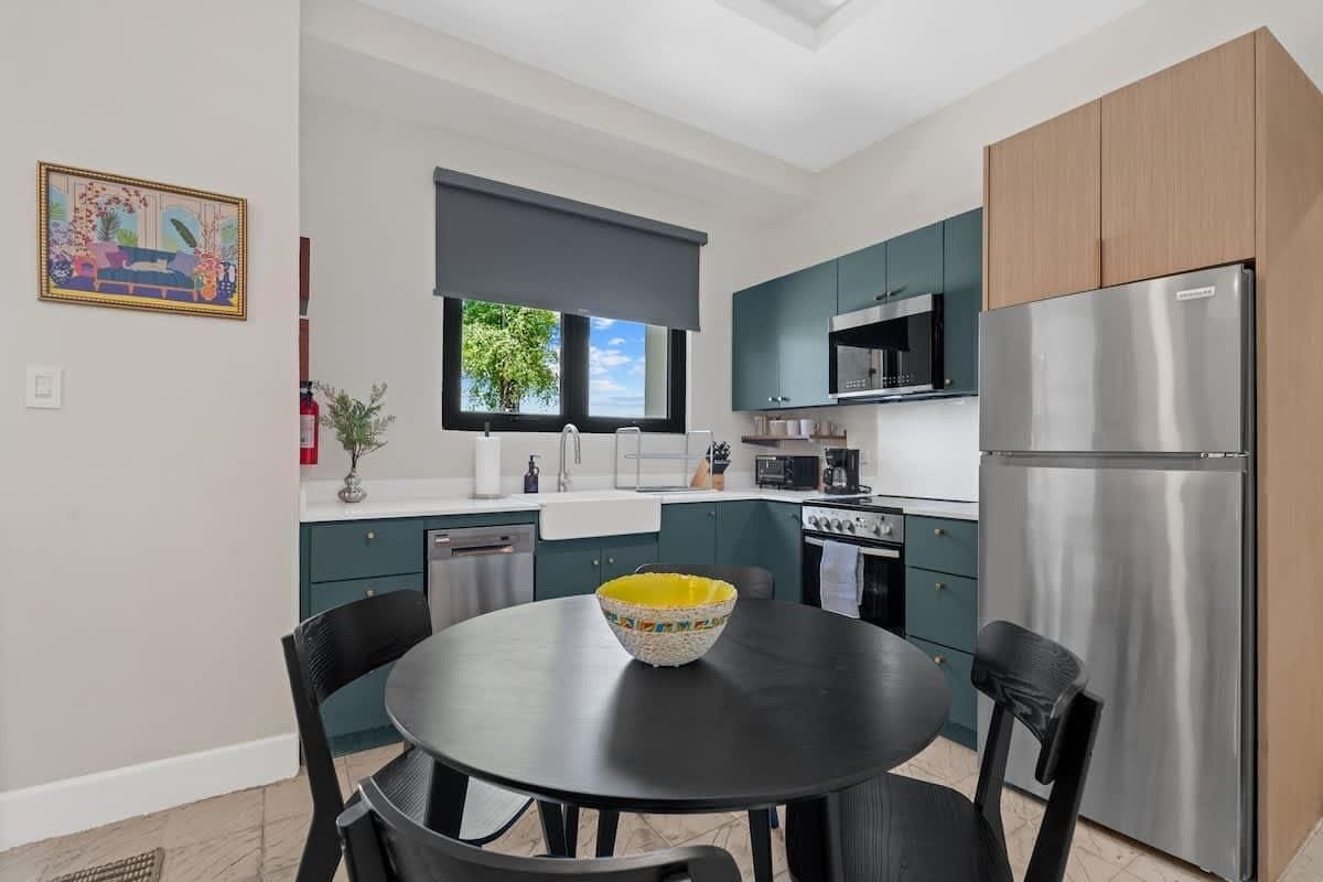 A modern kitchen with a dining table, chairs, a refrigerator, and a window with a view.