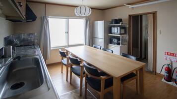 A compact kitchen with a dining table, chairs, a refrigerator, microwave, and a fire extinguisher.