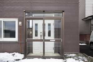 A glass door entrance to a building with a brick facade, a window to the left, and a car parked nearby.