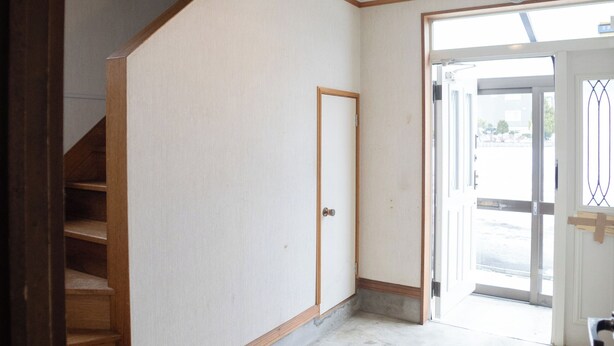 Um quarto com escada de madeira, uma porta e vista através de uma porta aberta.