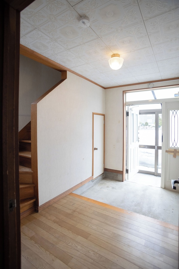 A room with a wooden staircase, a door, and a view through an open door.