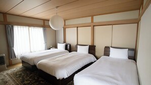 Quarto de hotel com duas camas, uma janela grande com cortinas, um lustre e um tapete estampado.