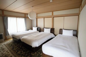 A hotel room with two beds, a large window with curtains, a hanging light fixture, and a patterned rug.