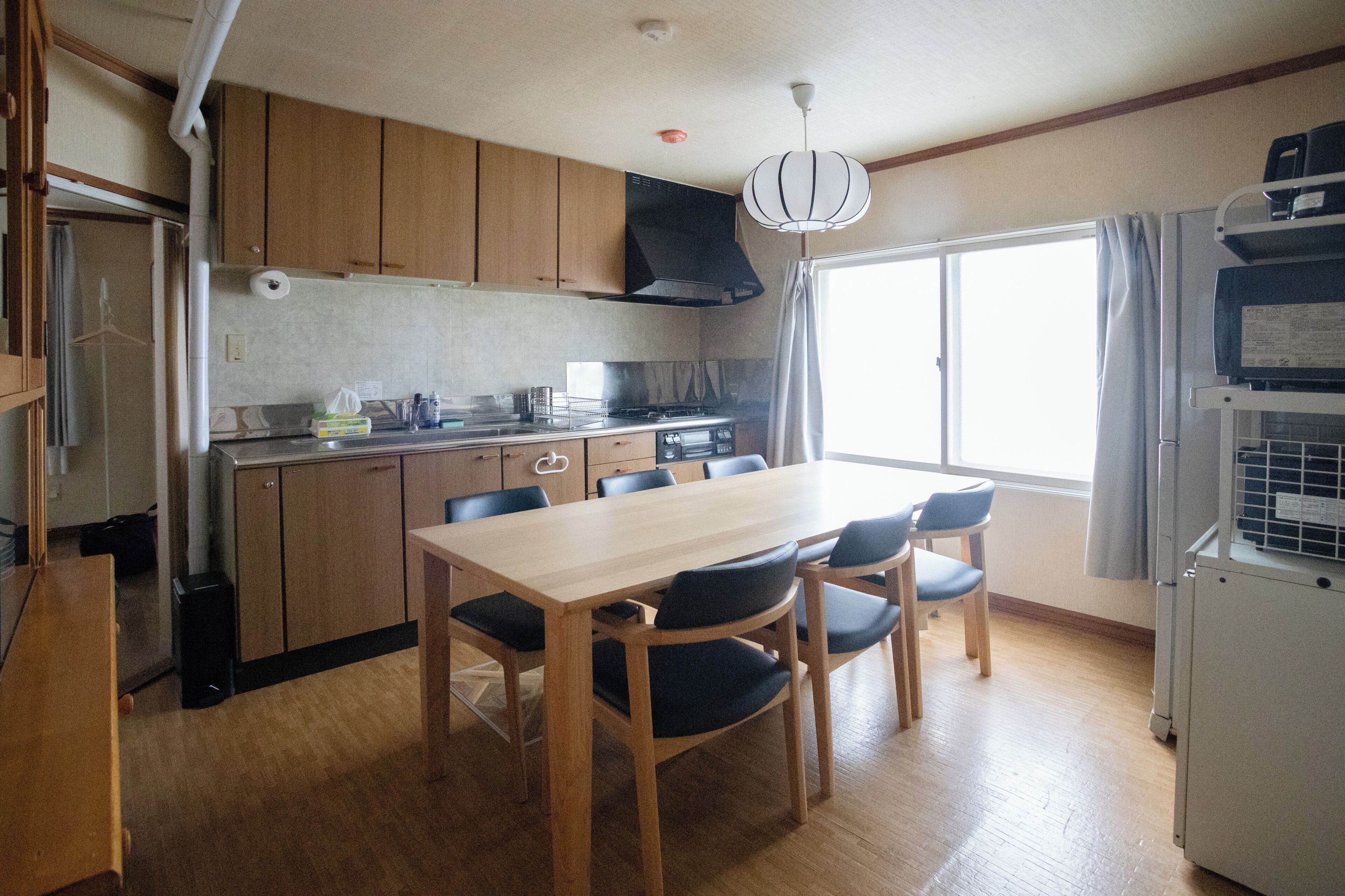 A compact kitchen with wooden cabinets, a dining table with chairs, a built-in stove, and a window with curtains.