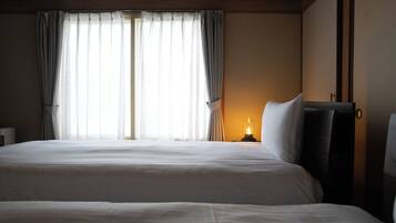 A hotel room with two beds, a nightstand with a lamp, and a window with curtains.