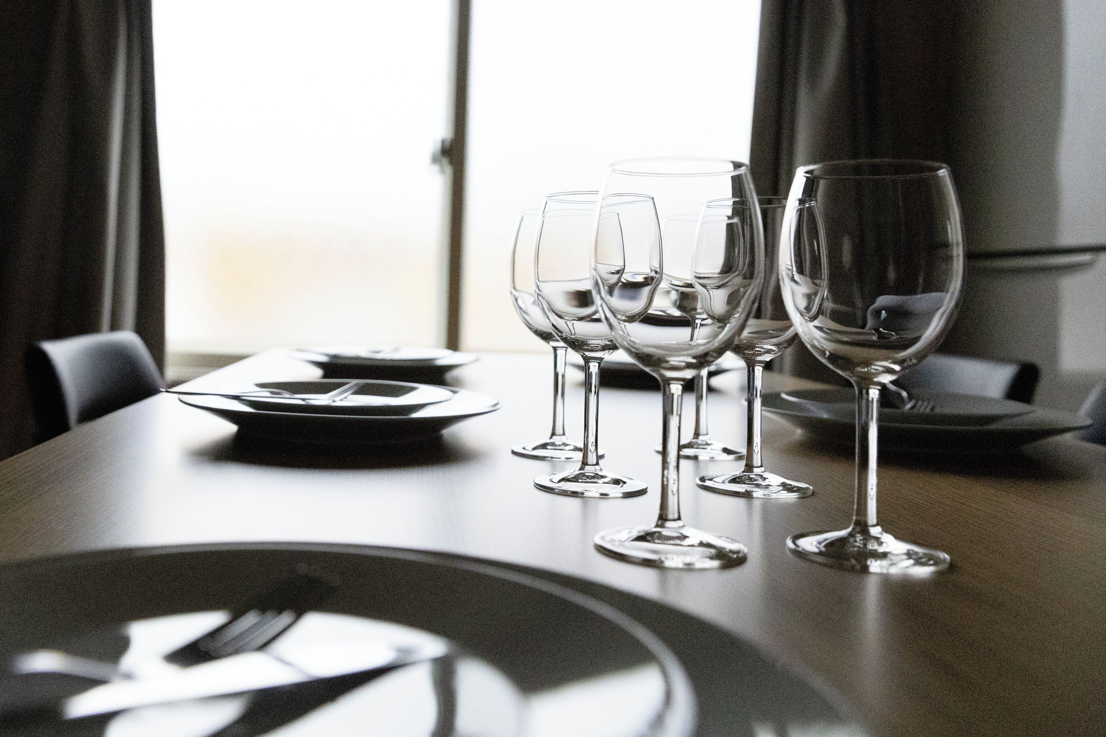 A dining table with multiple wine glasses and plates, set in a room with a window and curtains.